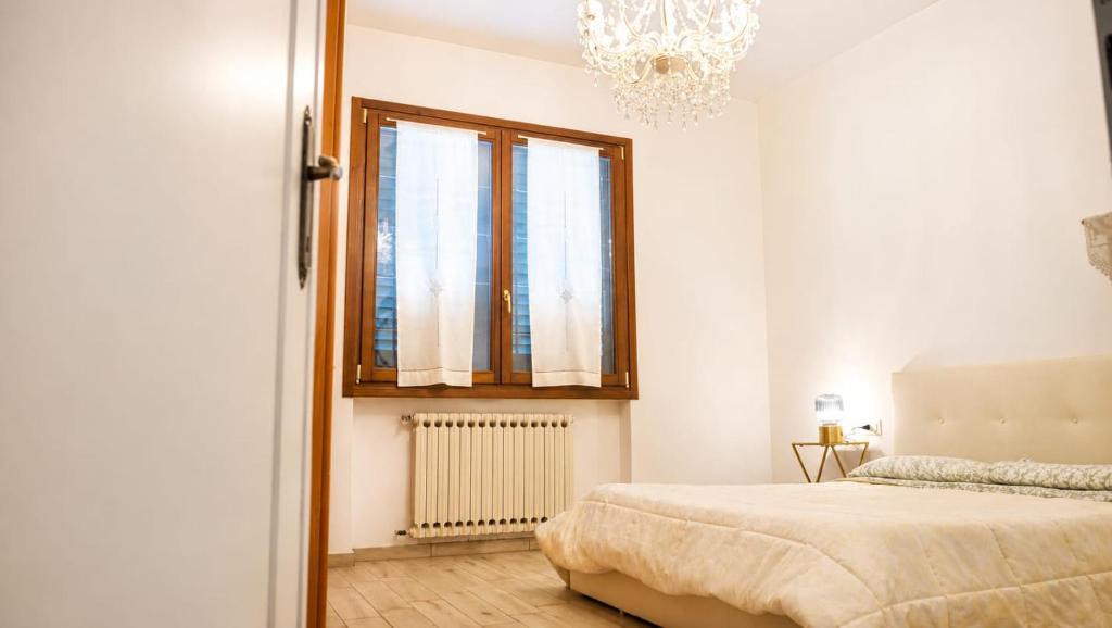 A bright bedroom with a large bed, window, radiator, chandelier, and bedside table.