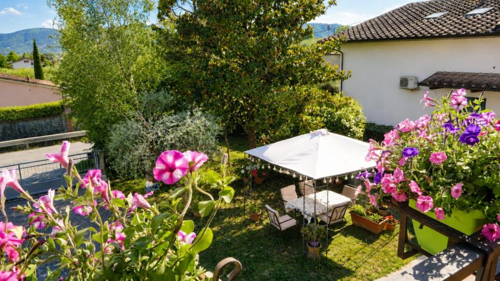 A garden seating area with a white umbrella and flowers, framed by trees, a house, and distant mountains.