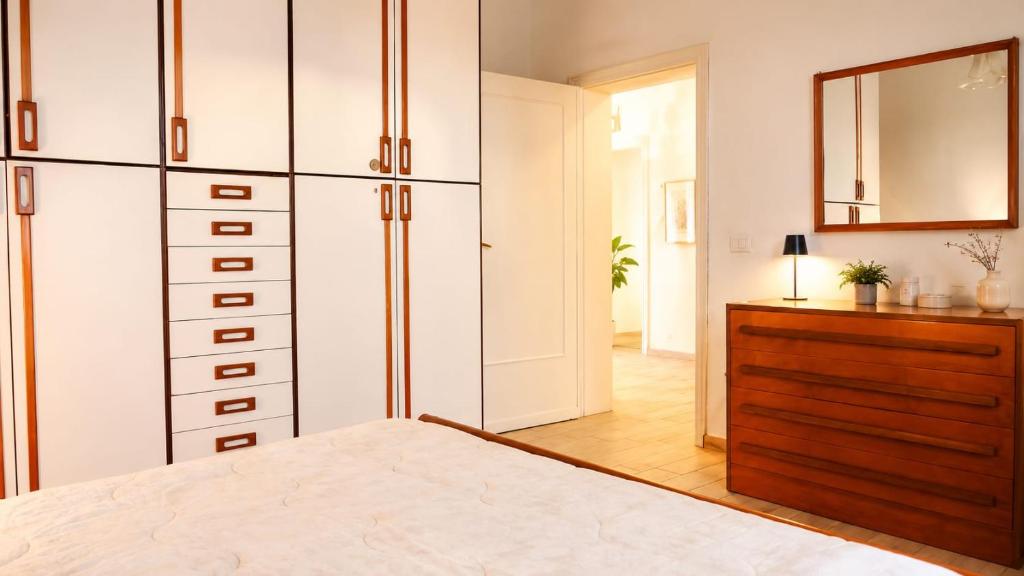 A bright bedroom with a large bed, built-in wardrobes, a wooden dresser, mirror, and an open doorway.